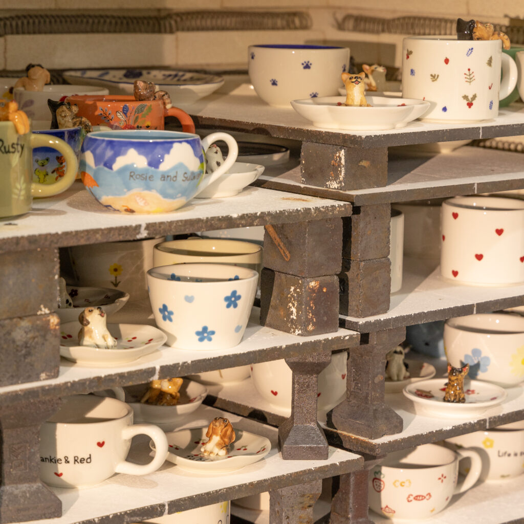 Custom porcelain cups and small figurines displayed on studio shelves
