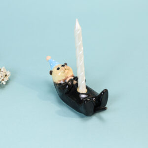 Cute otter ceramic cake topper candle holder with blue party hat and lit birthday candle