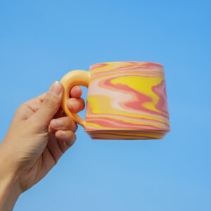All Things Flourish marbled ceramic mug with rounded yellow handle in pink peach and yellow tones